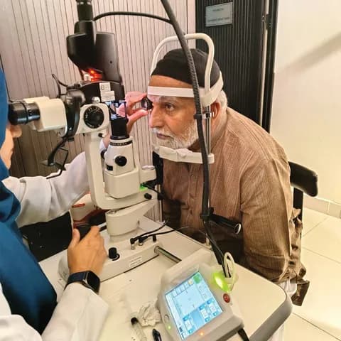 An elderly man undergoing an eye examination using a slit lamp, assisted by a female doctor.