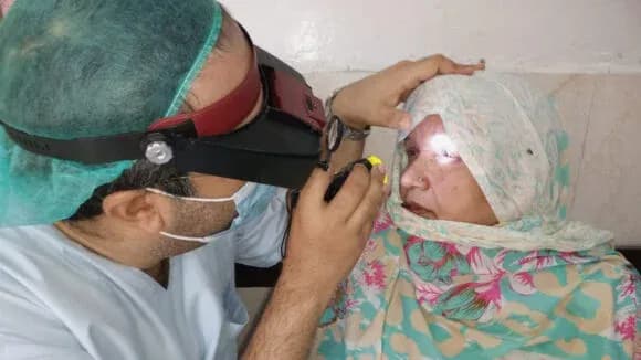 Doctor performing an eye examination on a woman wearing a headscarf using a specialized magnifying tool