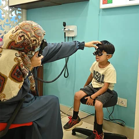 An eye doctor conducting an eye examination on a young boy using an ophthalmoscope.