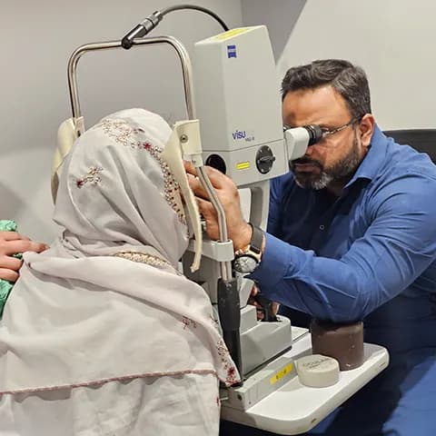A doctor performing an eye examination on a woman using a slit lamp.